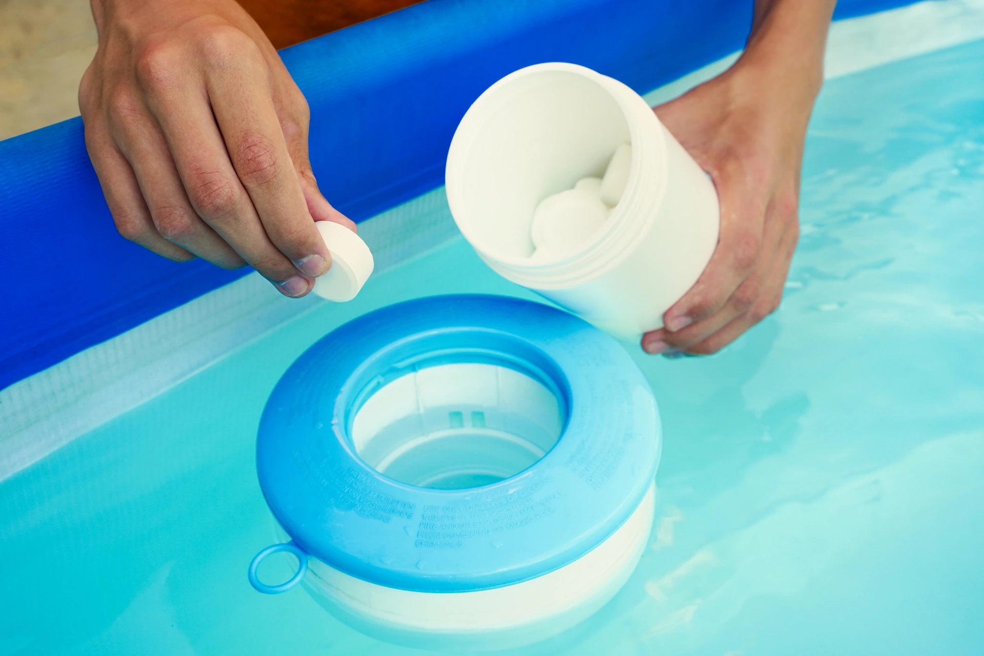 Close up on a pool owner's hand placing a chlorine tablet into a floating chlorine receptacle. With the rise of alternative sanitation products, the chlorine shortage has diminished.
