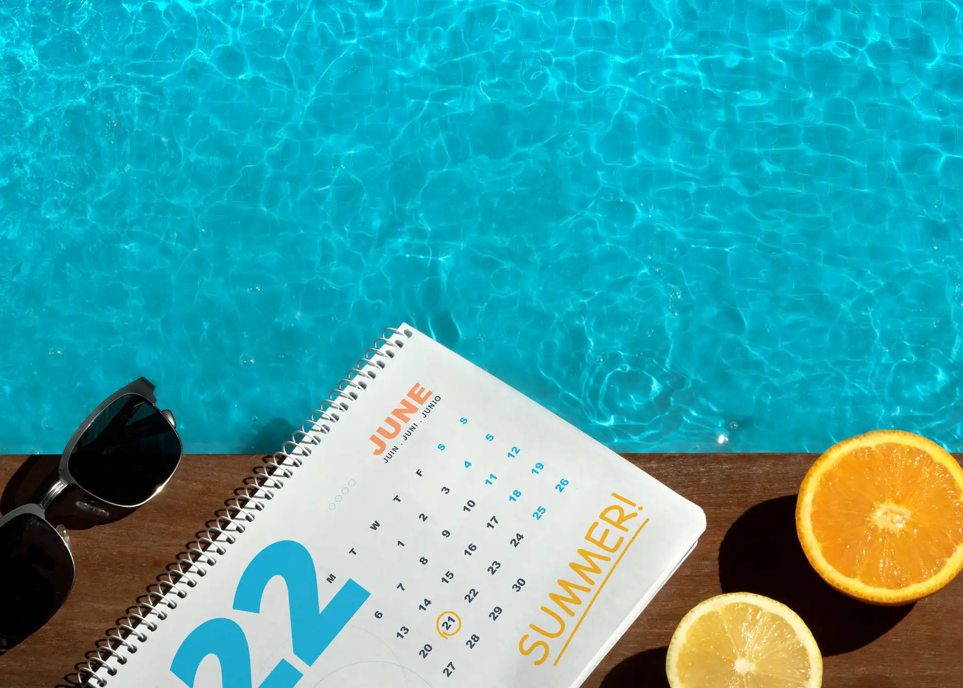 A calendar, a pair of sunglasses, and a halved orange sit at the edge of an inground pool in the daylight. When scheduling new projects, it benefits pool builders to have a waitlist to maintain engagement with potential customers.