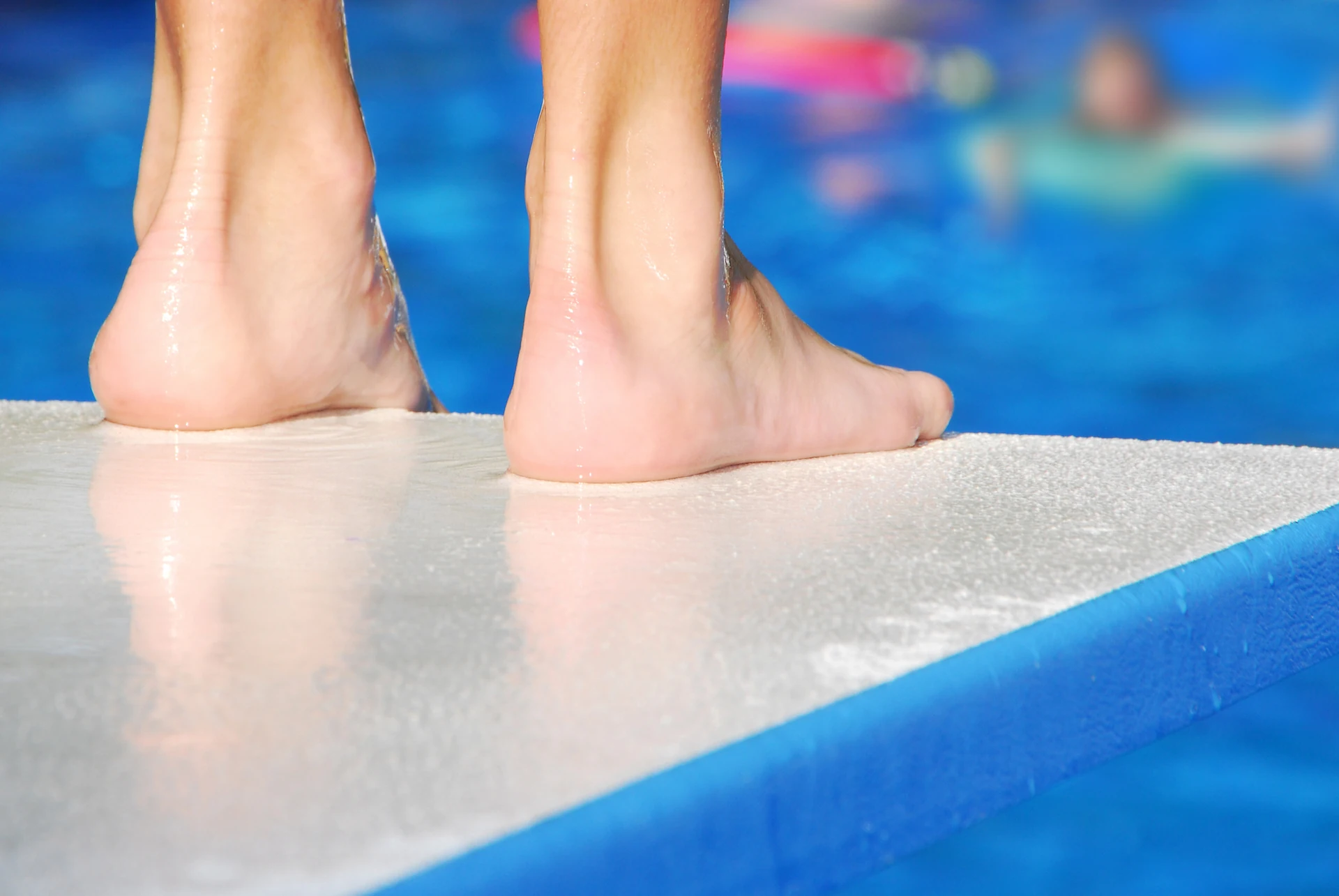 Close-up of a person's feet as they stand at the edge of a diving board. Pool safety tips are essential to pool customers, especially when using a pool like this.