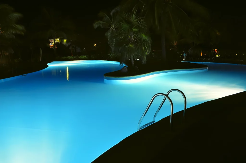 An inground pool illuminated at night by various pool lighting products.