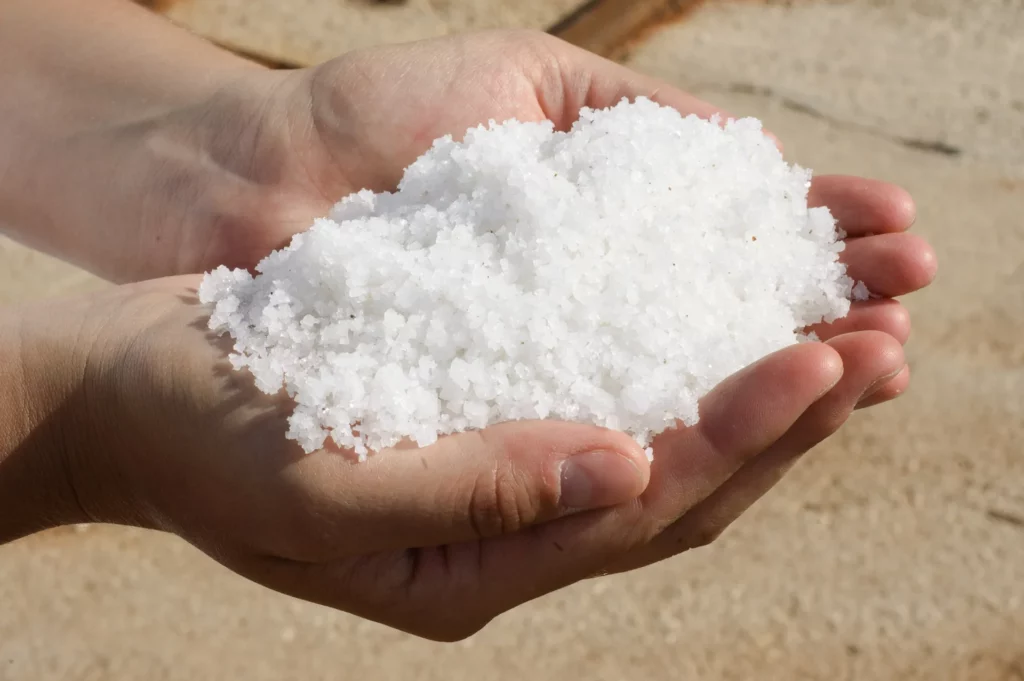 Close up on someone's hands as they hold a scoop of pool salt. Pool salt systems are growing in popularity as an alternative to traditional chlorine.