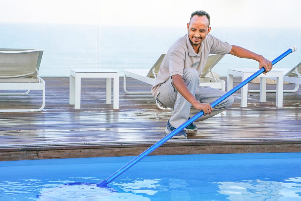 A pool service professional using a net to clean the surface of a pool.
