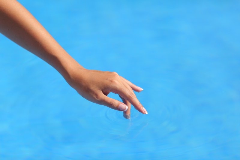 A woman's hand is hovering above the water. She is gently touching the water with one finger.