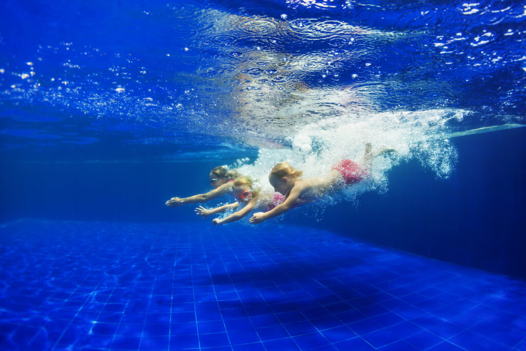 Three children are diving into a blue pool.